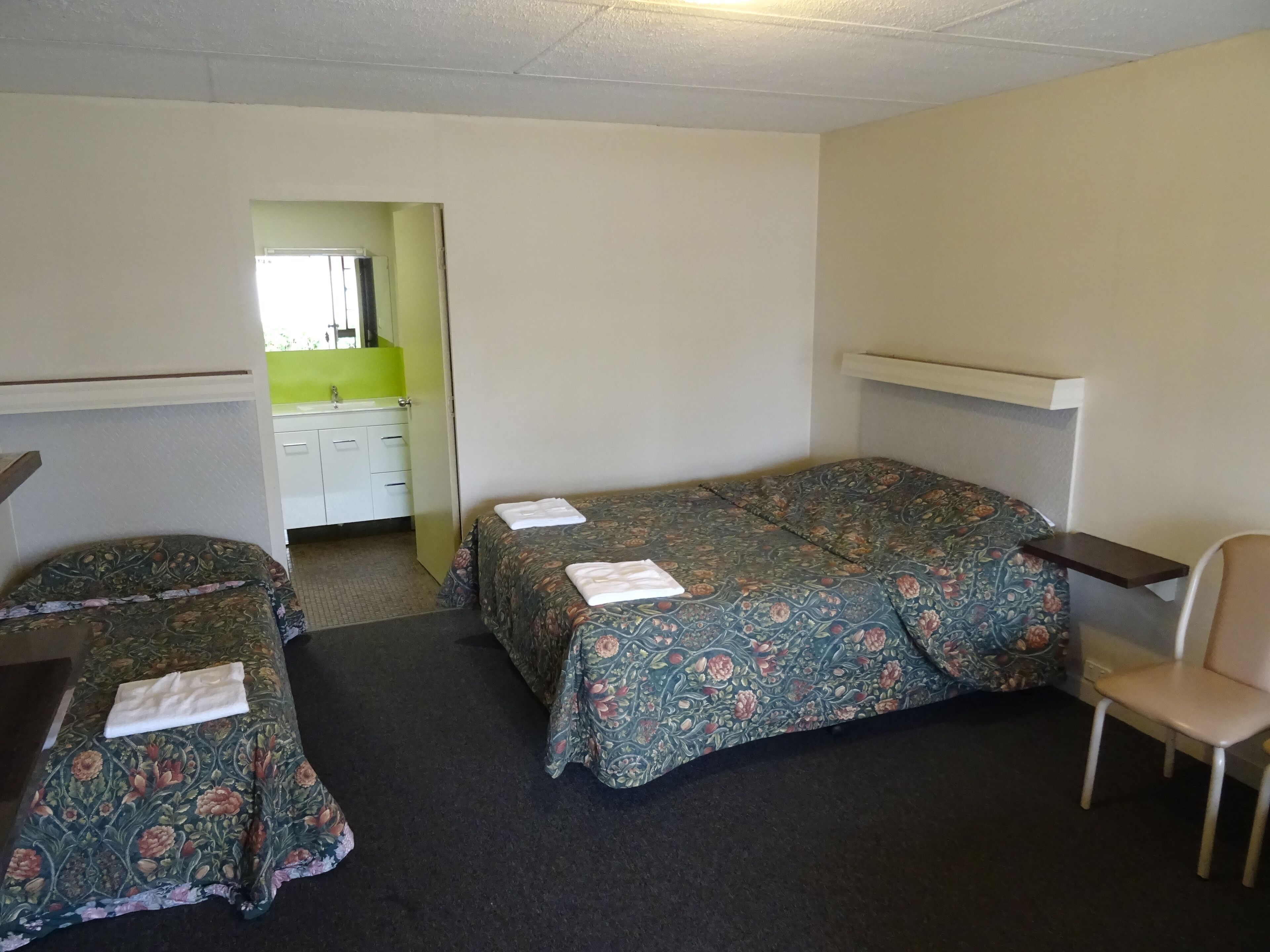 Habitación de hotel con dos camas, una silla, un escritorio y un baño visible a través de una puerta abierta.