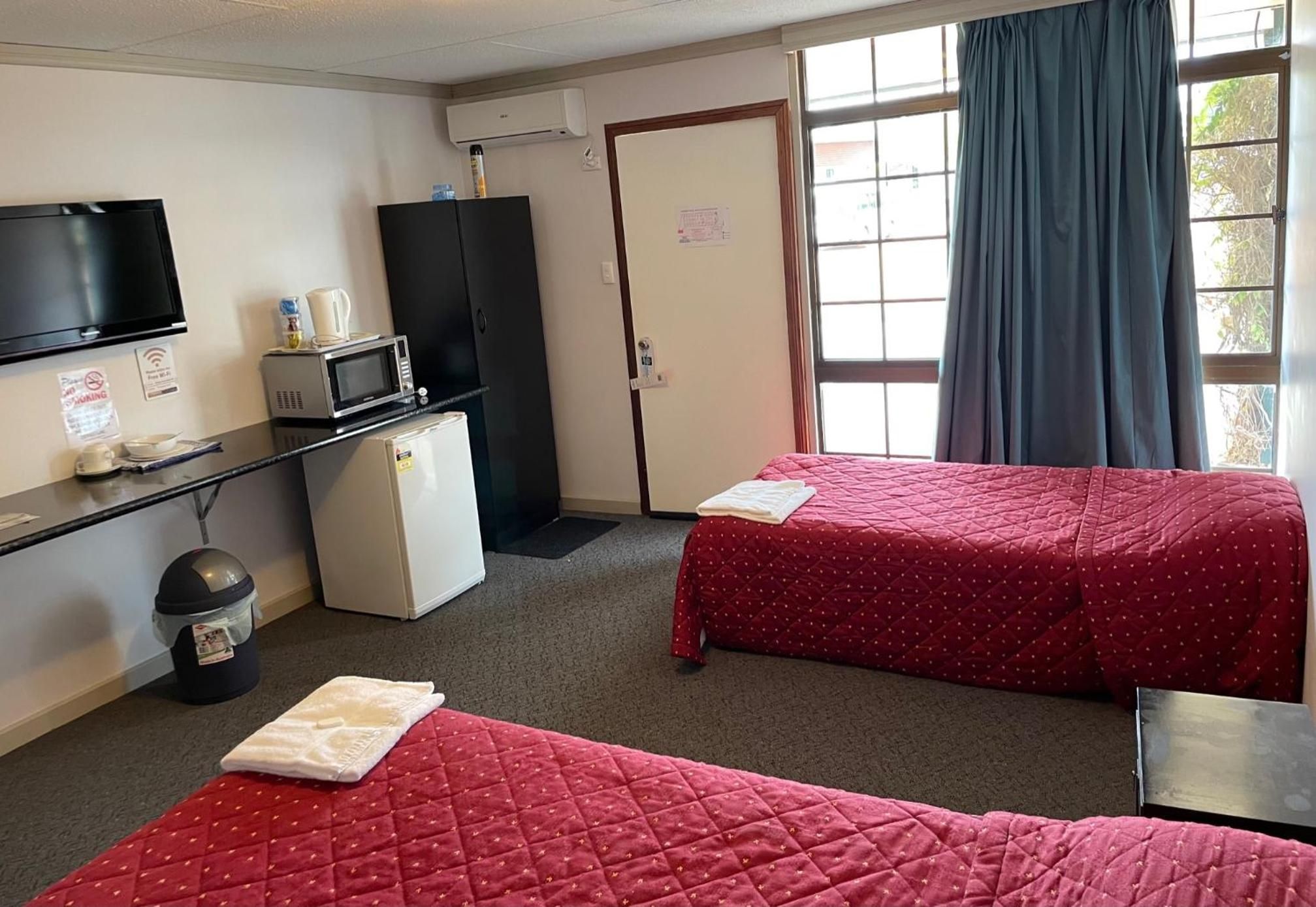 A hotel room with two beds, a desk with a microwave, a small refrigerator, a TV, and a window with curtains.