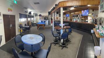 A bar area with a pool table, seating, and a counter with various items.
