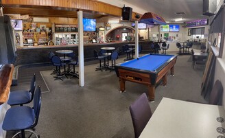 Una sala de billar con mesas de pool, sillas y una zona de bar con televisión.