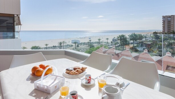 Un balcon avec des éléments pour le petit-déjeuner, une vue dégagée sur la plage et un panorama sur la ville côtière.