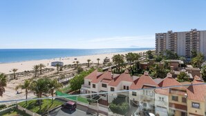 Une vue côtière avec une plage, des palmiers et des immeubles résidentiels aux toits recouverts de tuiles rouges.