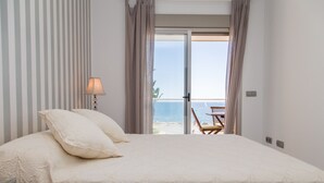 Ein Schlafzimmer mit Bett, Lampe und Meerblick durch eine Schiebetür.