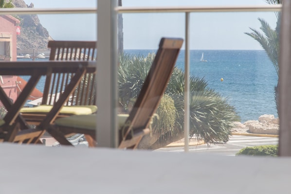 A view from a window overlooking a beach with a sailboat, palm trees, and a rocky coastline.