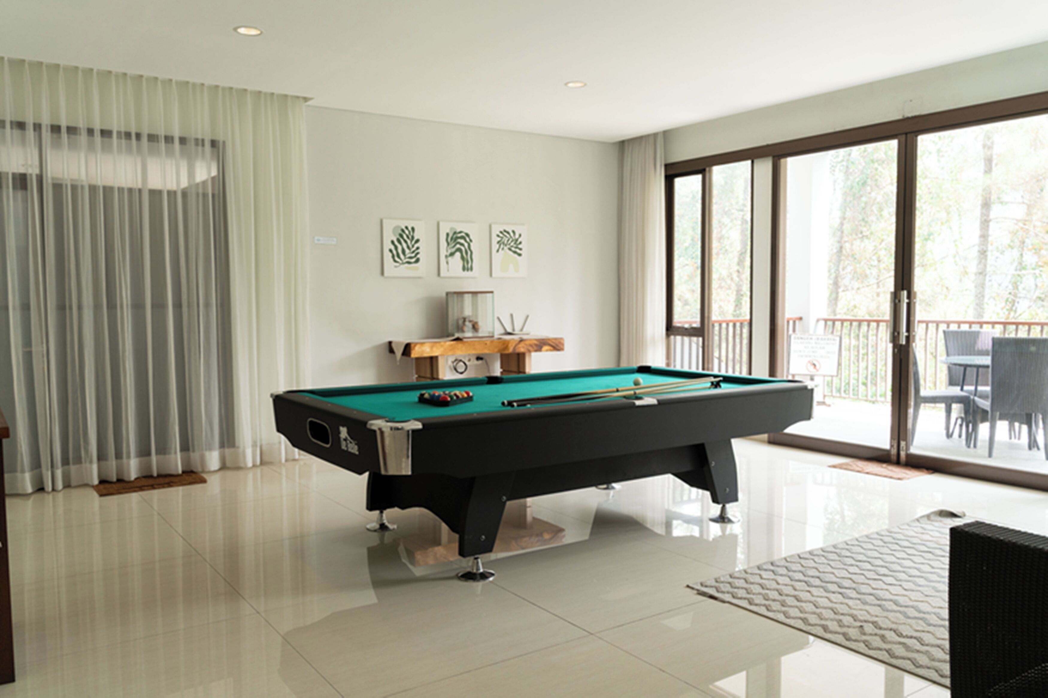 A pool table in a room with a large window, curtains, and three framed artworks on the wall.