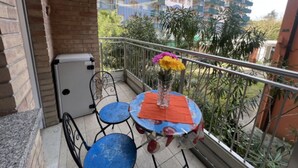 Un balcon avec une table et des chaises, un pot de fleurs et une vue sur un immeuble à plusieurs étages.