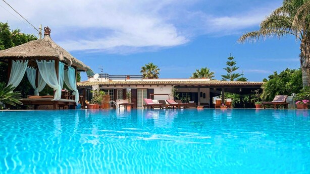 A clear blue swimming pool with lounge chairs and a thatched-roof structure. - **** RUMAH SAYA ****  Balinese house by the sea (Campofelice di Roccella)