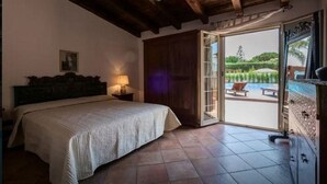 A bedroom with a bed, a nightstand, a wooden headboard, and a view of a swimming pool through an open door. - **** RUMAH SAYA ****  Balinese house by the sea (Campofelice di Roccella)
