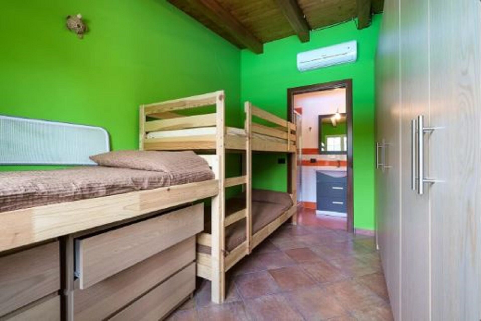 A room with bunk beds, a wooden wardrobe, and a green wall.