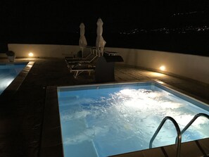 An outdoor swimming pool with hot tub, lounge chairs, and umbrellas.