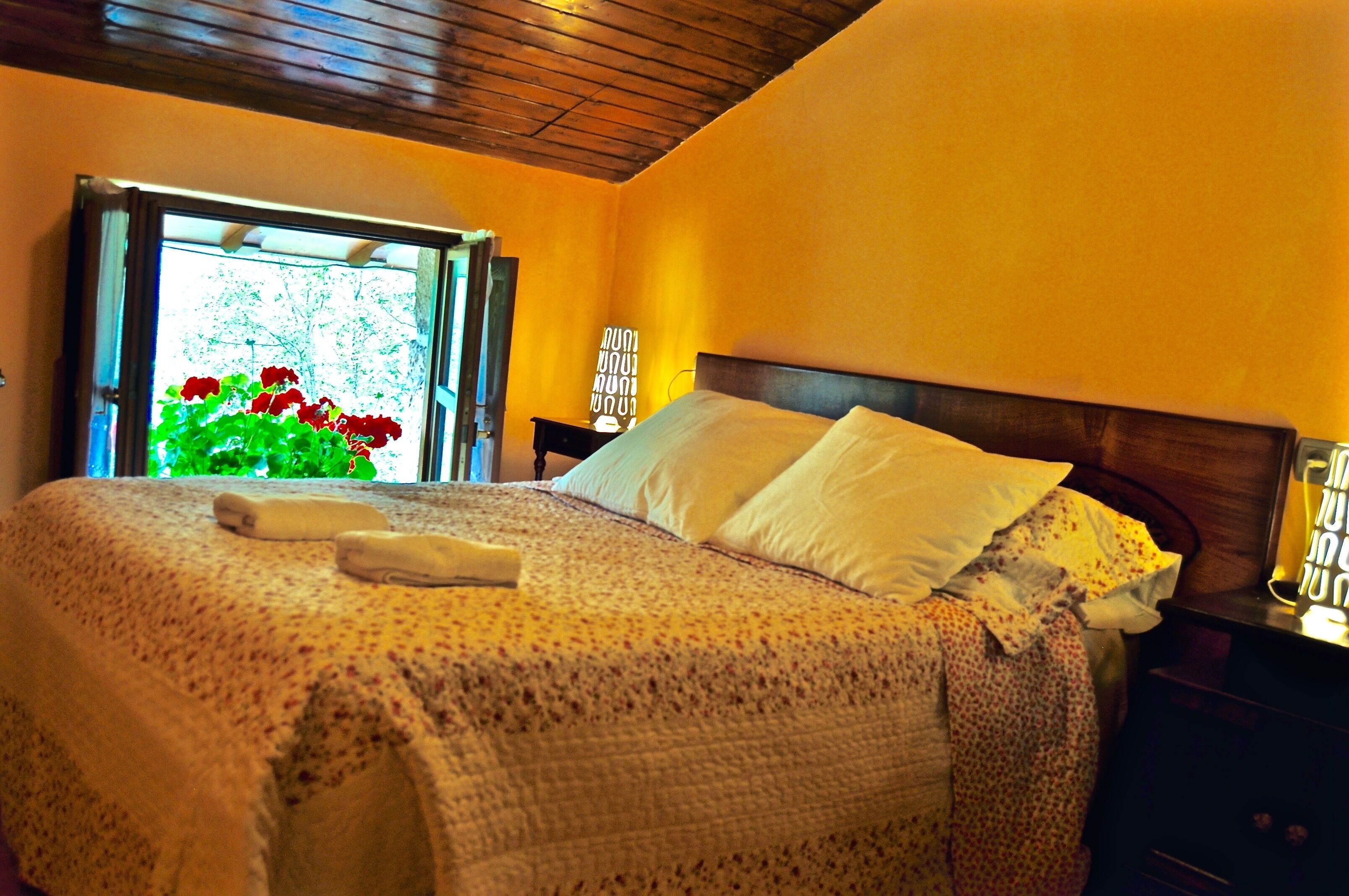 A neatly made bed with a floral-patterned bedspread and pillows, a wooden headboard, and a nightstand with a lamp.