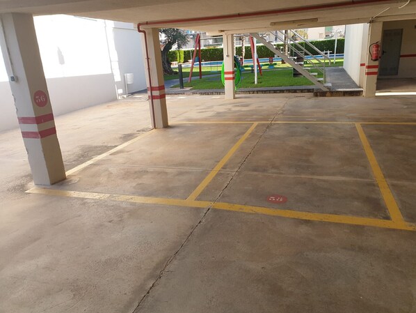 Un espace de stationnement couvert, doté d’un sol en béton et de lignes jaunes délimitant les places de stationnement.