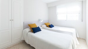 A hotel room with two single beds, a wardrobe, a window with blinds, and a wall-mounted light fixture. - Beautiful condo family near to the beach. Pool / Wifi - only families (Playa de Gandía)
