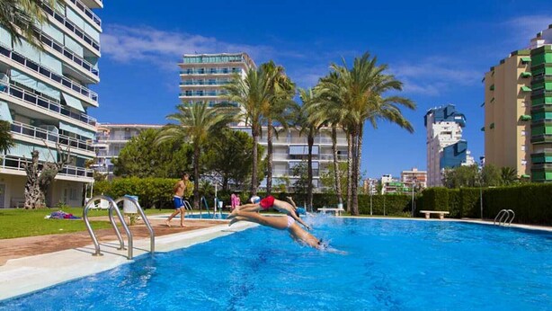 A swimming pool with a person diving, surrounded by palm trees and modern buildings. - Beautiful condo family near to the beach. Pool / Wifi - only families (Playa de Gandía)