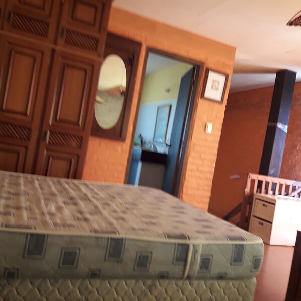 A room with a mattress, wooden wardrobe, and a door leading to another room.