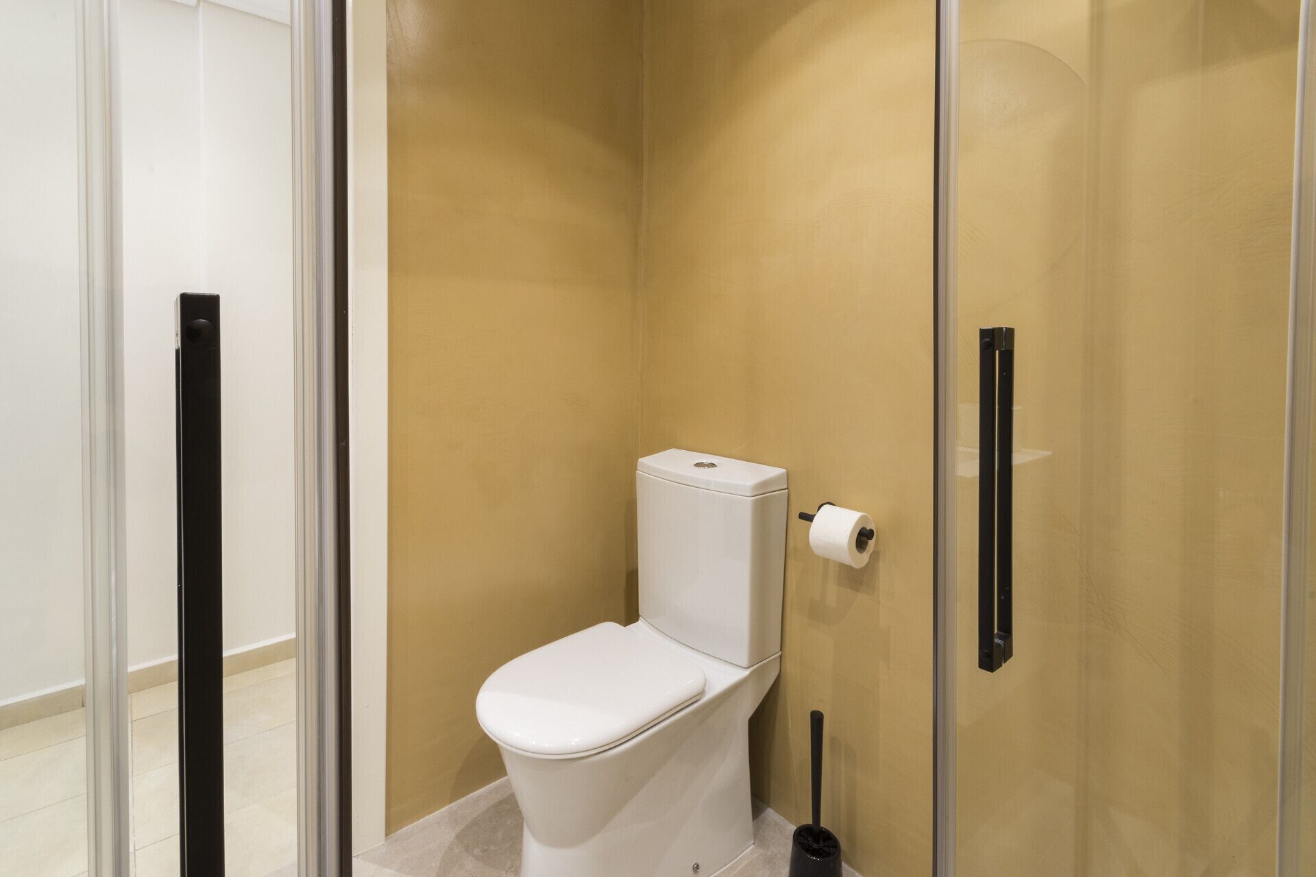Un baño moderno con cabina de ducha de vidrio, un inodoro blanco y un dispensador de papel higiénico.