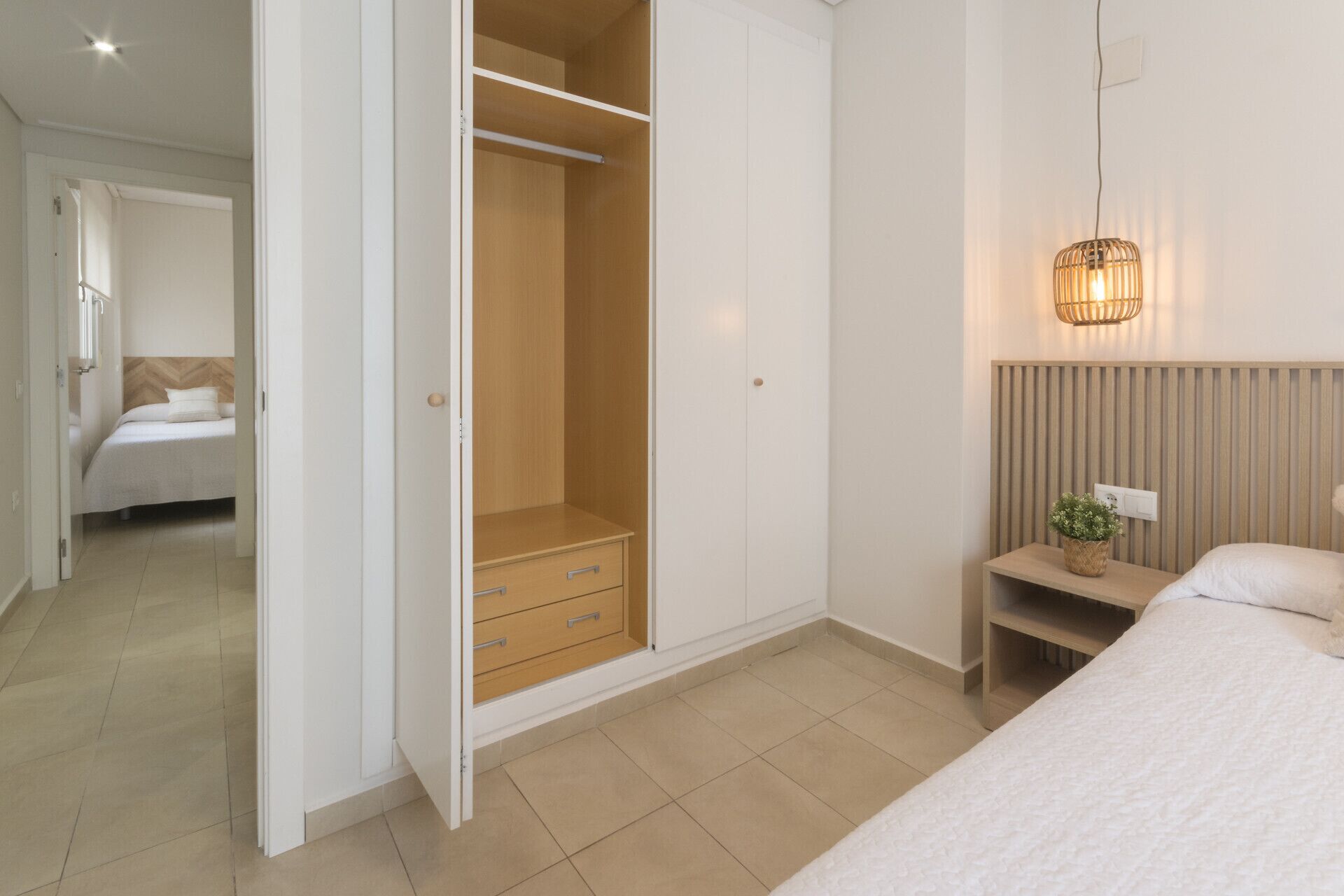 A bedroom with a bed, bedside table, lamp, and a walk-in closet with drawers.