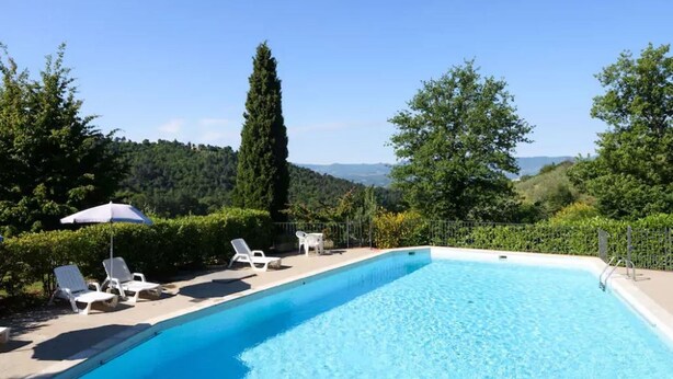 Une piscine d’un bleu éclatant, dotée de chaises longues et d’un parasol, entourée de verdure et avec des collines en arrière-plan.