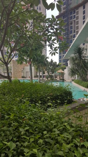 A pool area with surrounding greenery and a building in the background. - Wales Swiss Garden Residence (Kuala Lumpur)