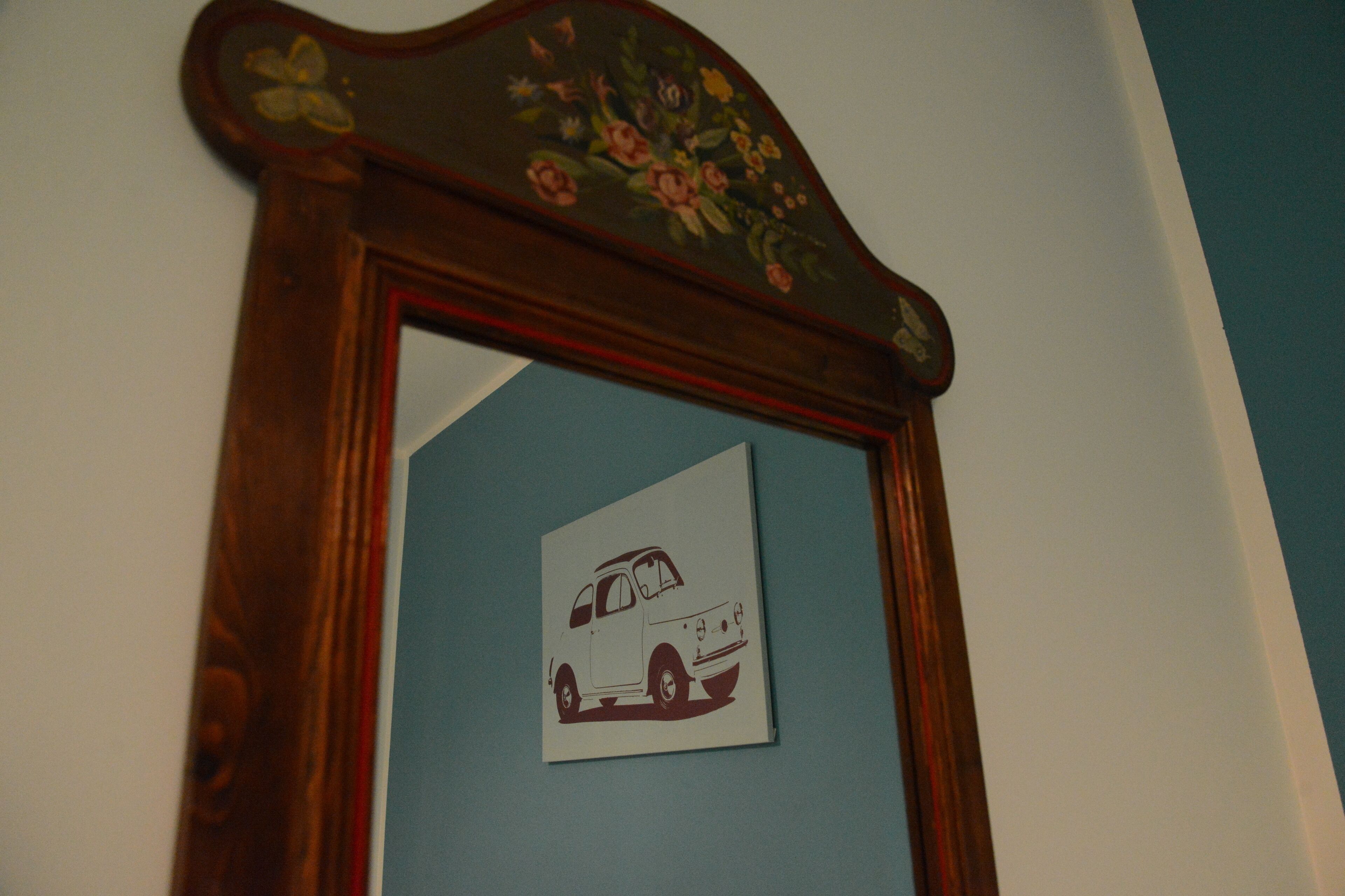 A mirror with a floral design on the top and a picture of a car on the mirror's surface.