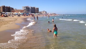A beach with people swimming and walking along the shore, umbrellas, and buildings in the background. - Modern villa with large garden and close to the sea (Catral)