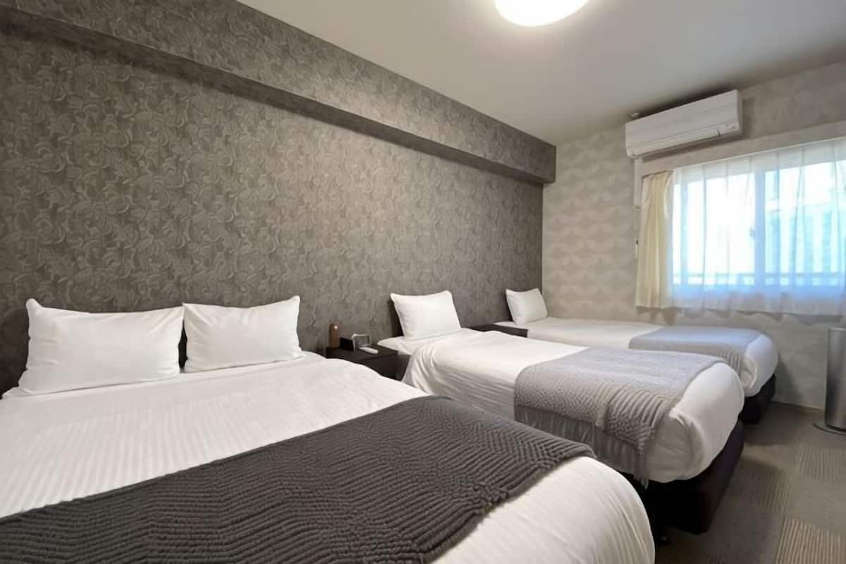 A hotel room with three beds, a large window with curtains, and a wall-mounted air conditioner.