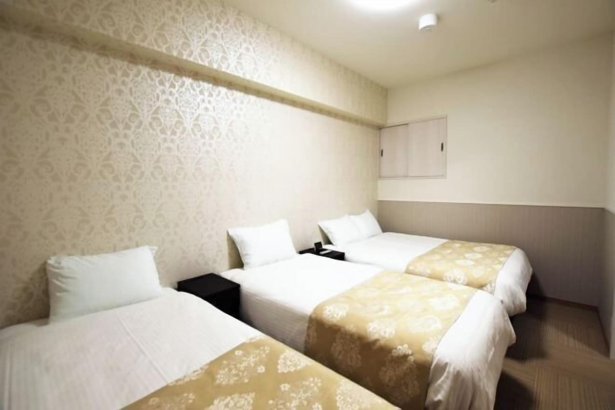 Habitación de hotel con tres camas, un papel tapiz estampado y un techo liso.