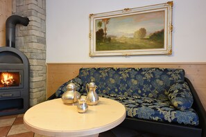 A cozy living room with a stone fireplace, a sofa with floral upholstery, and a table with silver tea sets.