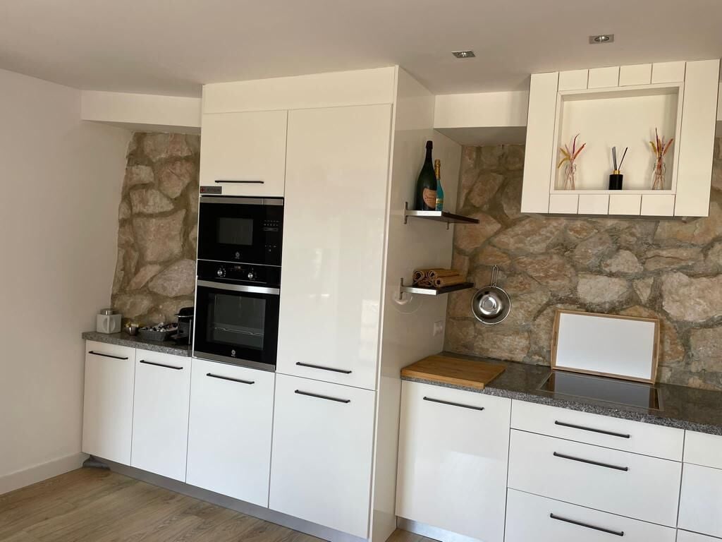 Een moderne keuken met witte kasten, een inbouwoven en een wand met stenen accenten.