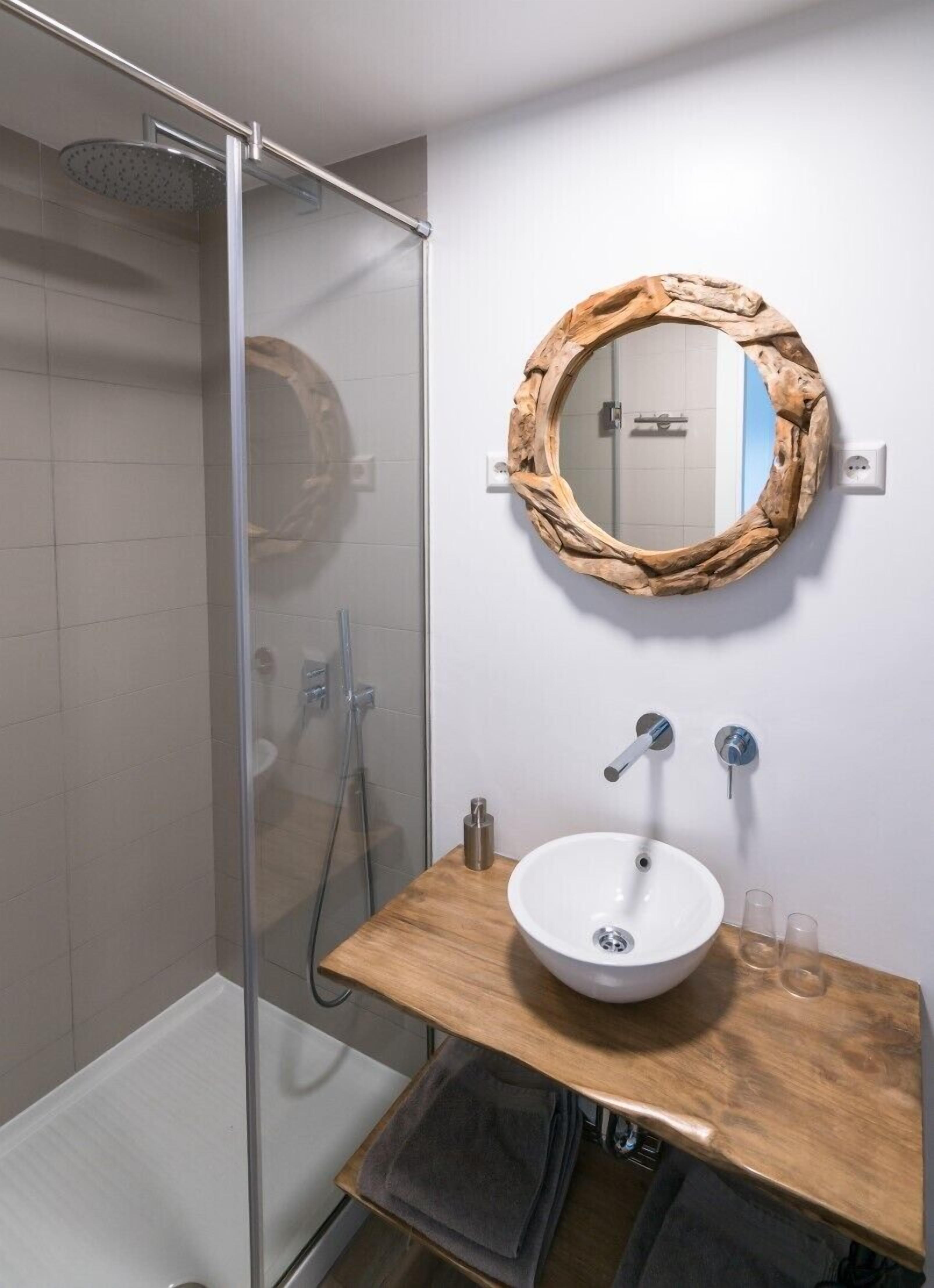A bathroom with a glass-enclosed shower, a wooden vanity with a white sink, and a mirror with a natural wood frame.