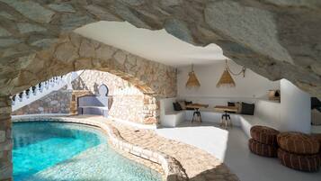 Ein Pool mit Steinwänden und unendlichem Wasserrand, ein Sitzbereich am Pool ebenfalls mit weißem Wasserrand, und ein steinernes Tor.