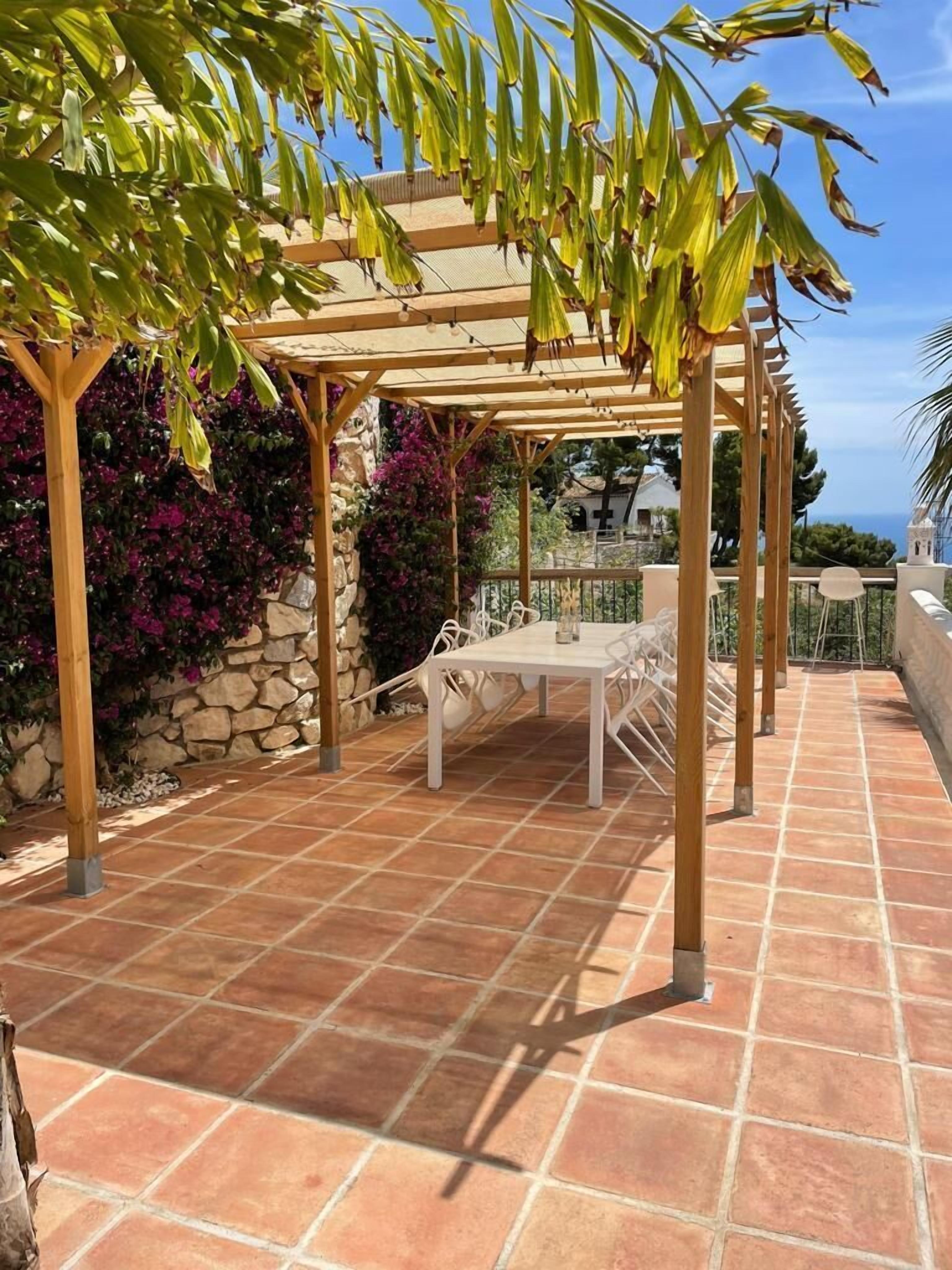 Una veranda coperta con una pergola, un muro in pietra e un tavolo con sedie.