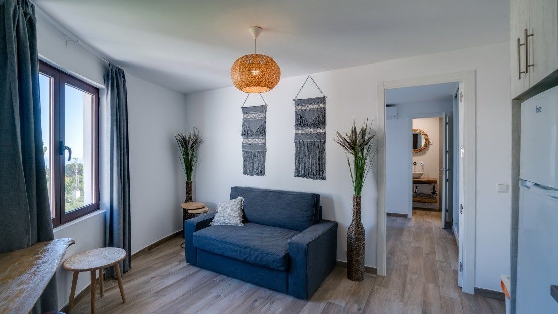 A modern living room with a blue sofa, a round hanging light, and two wall-mounted macramé decorations.