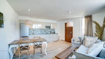 A modern kitchen with white cabinets, a dining table with chairs, and a sofa with patterned cushions.