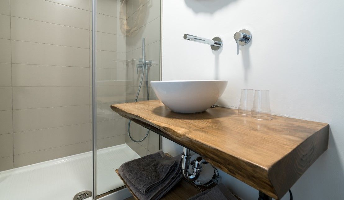 Un bany modern amb un tocador de fusta, un lavabo blanc i una cabina de dutxa de vidre.