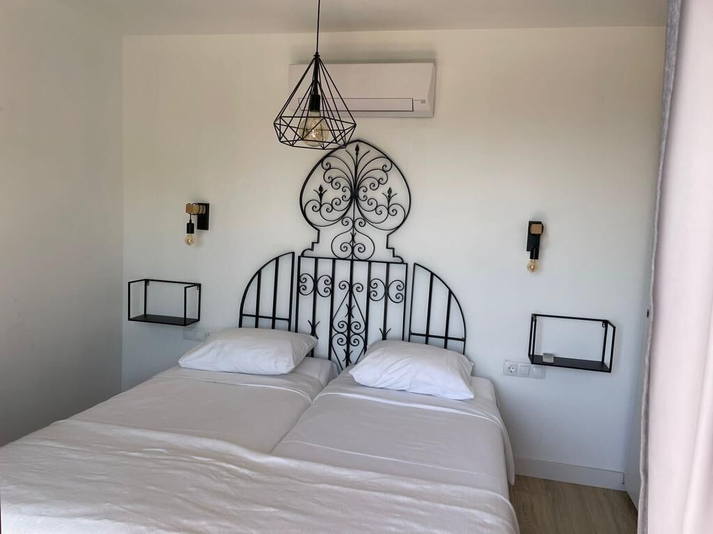 A double bed with a decorative headboard, two bedside tables, and a hanging light fixture.
