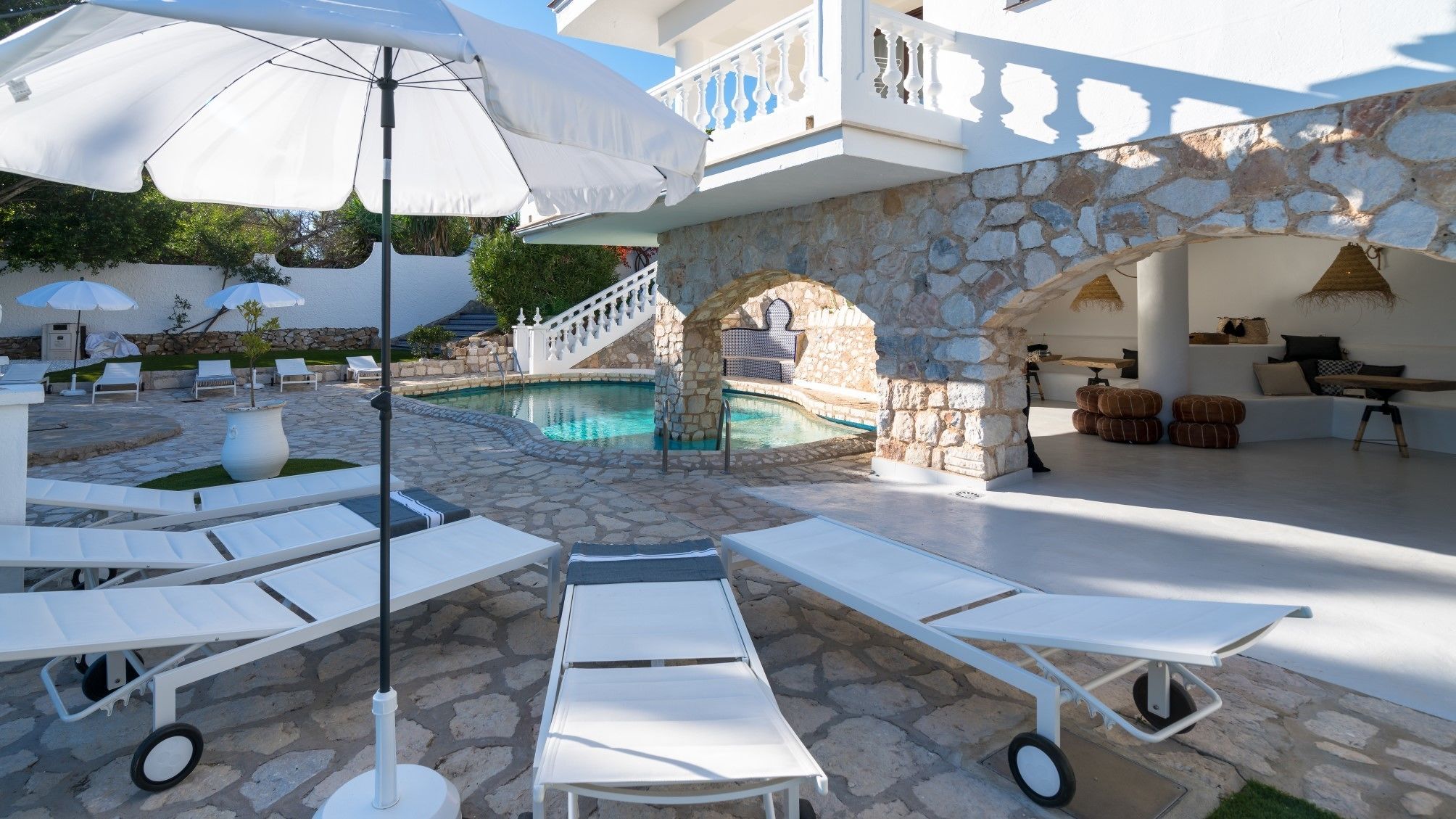 A poolside area with lounge chairs, umbrellas, and a stone wall.