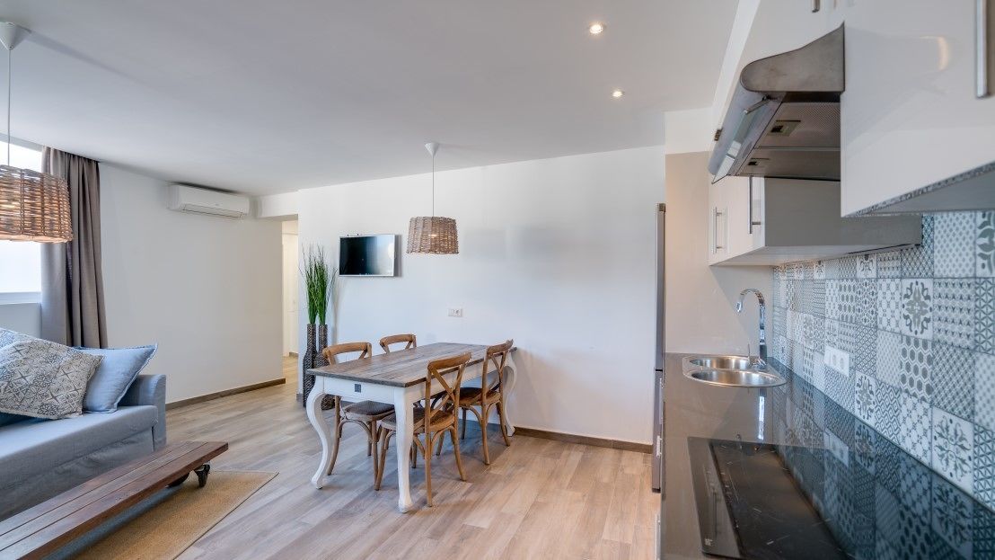 A modern kitchen with a dining area, a sofa, and a TV.