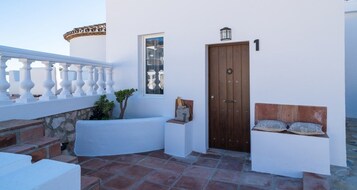 A white building with a wooden door, a balcony with white railings, and a stone wall.
