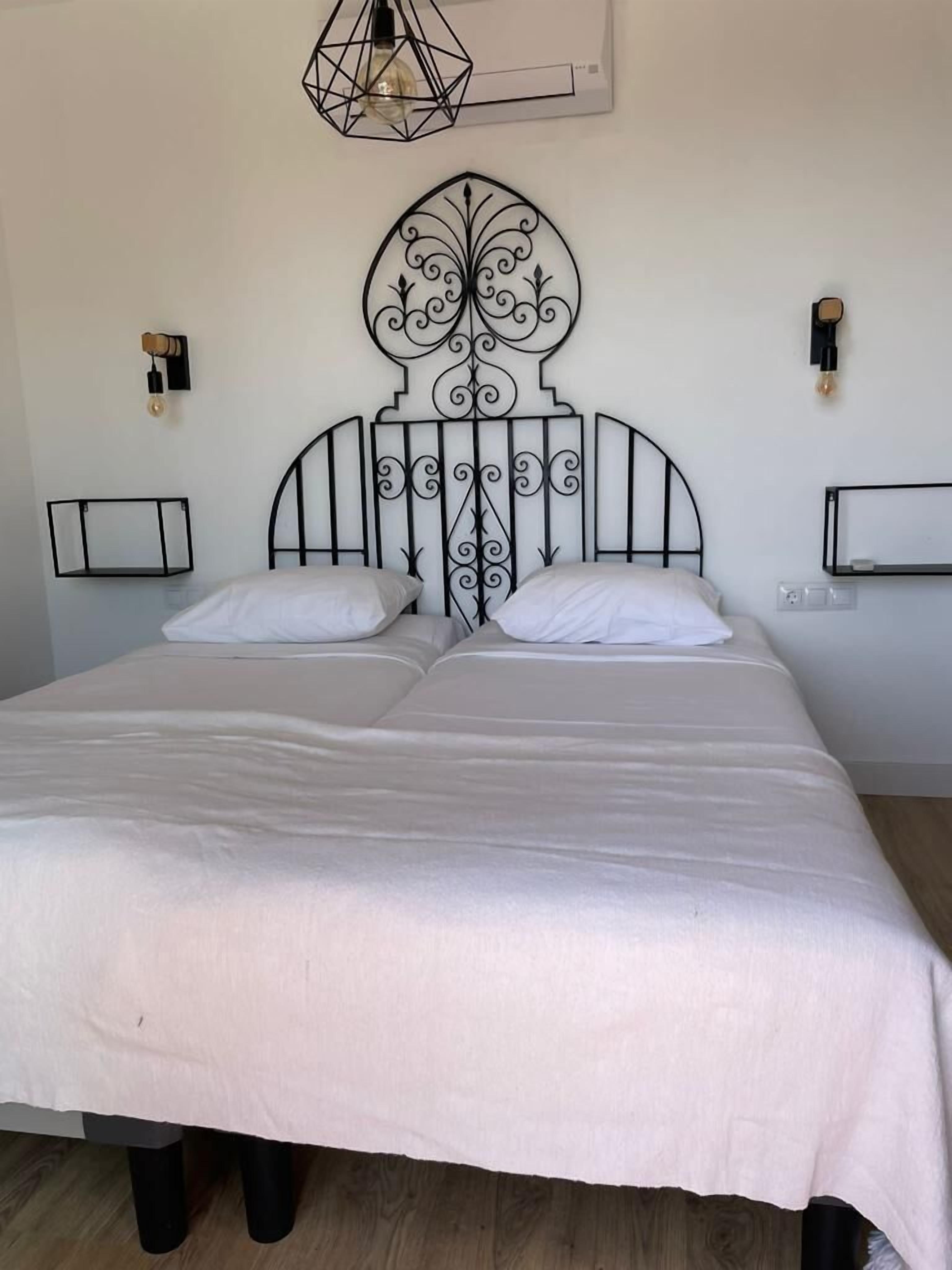A double bed with a decorative metal headboard, two bedside tables, and a hanging light fixture.