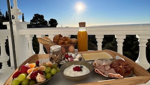 A breakfast tray with fruits, cheeses, and meats on a balcony with a white railing and a clear view of the sea. - Mijas Residence (Mijas)