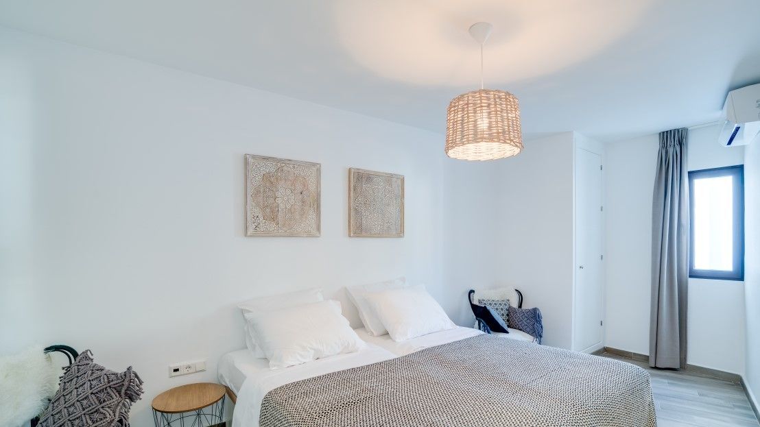 Ett modernt sovrum med en säng, två konstverk på väggen, en hängande lampa och ett fönster med gardiner.