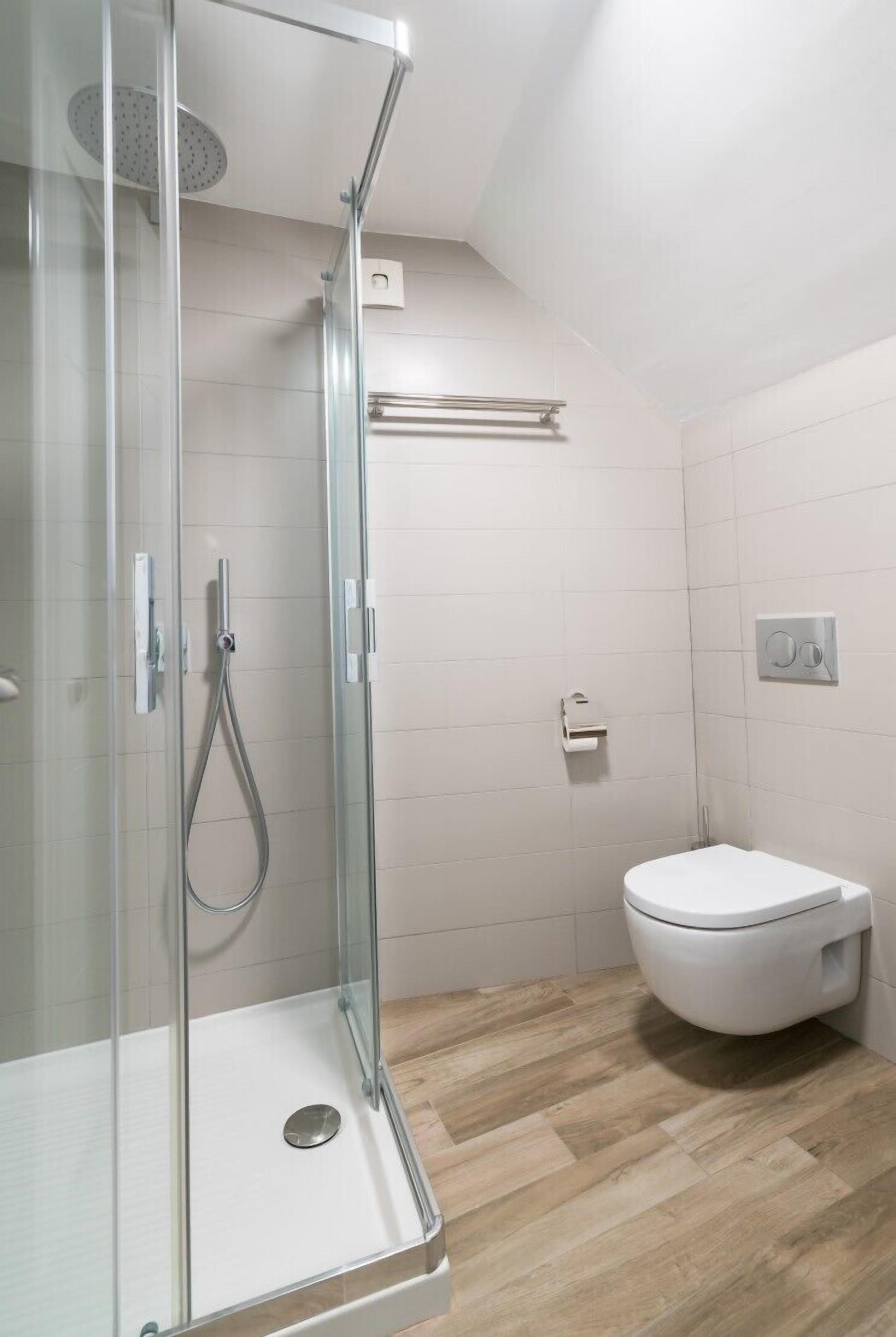 A modern bathroom with a glass-enclosed shower, a white toilet, and a wooden floor.