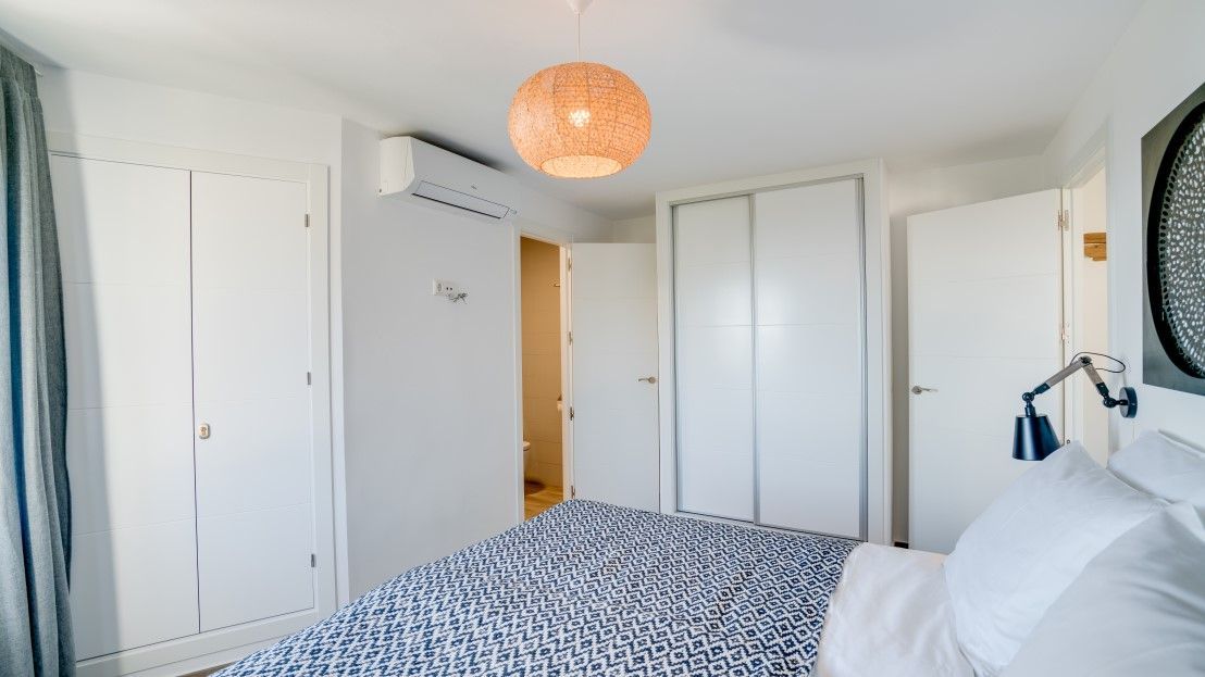 A bedroom with a patterned bedspread, white wardrobes, a hanging lamp, and a ceiling light fixture.