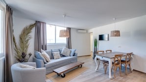 A modern living room with a sofa, a dining table with chairs, and a TV mounted on the wall. - Mijas Residence (Mijas)
