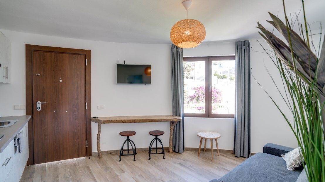 Eine moderne Küche mit Holztür, integriertem Fernseher, einem Holztisch mit Barhocker und einem großen Fenster mit Vorhängen.