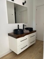 Ett modernt badrum med ett vitt handfatsskåp, en svart tvättställ och en stor spegel.