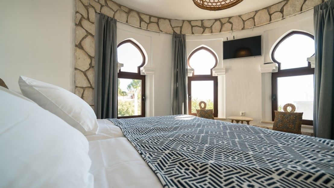 Une chambre à coucher avec un grand lit, des murs en pierre et des fenêtres en arc de cercle.