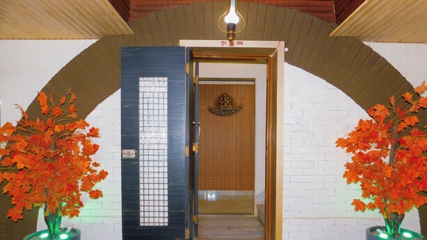 L’entrée d’un hôtel, avec une porte en bois, une petite statue de Bouddha et deux plantes en pot aux feuilles rouges.