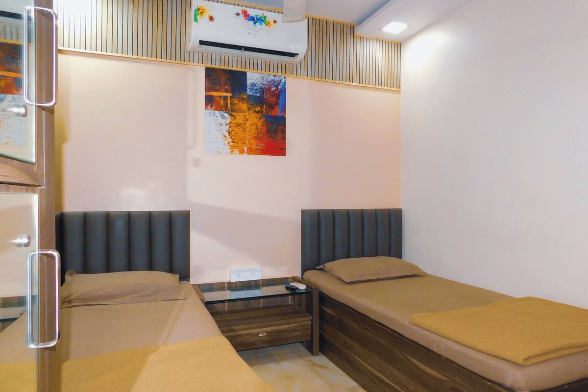 A small, modern room with two single beds, a glass table, and a wall-mounted air conditioner.